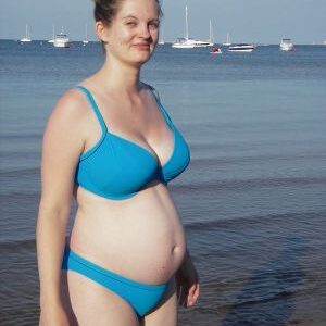 A pregnant woman in a bikini standing on a beach posing for the camera