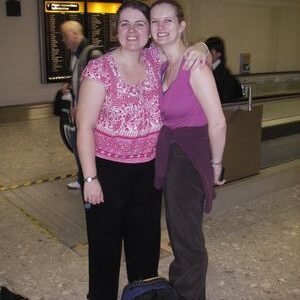 Two woman standing next to a bag of luggage at an airport