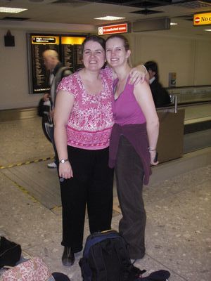 Two woman standing next to a bag of luggage at an airport