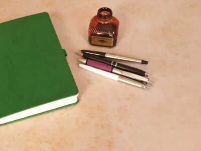 green journal with pens and a bottle of ink