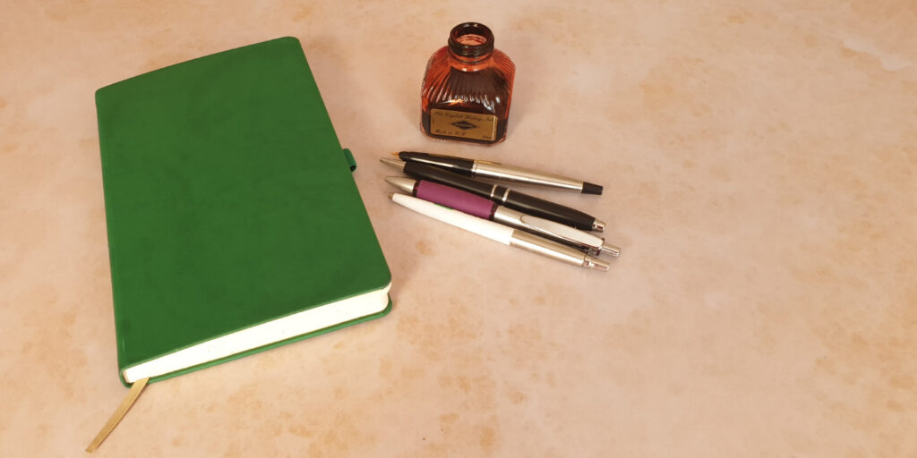 green journal with pens and a bottle of ink