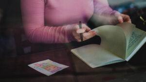 picture focused on the arms and hands of a woman wearing a pink jumper and flicking through a note book.