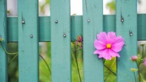 A pink flower growing through a green fence