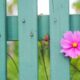 A pink flower growing through a green fence