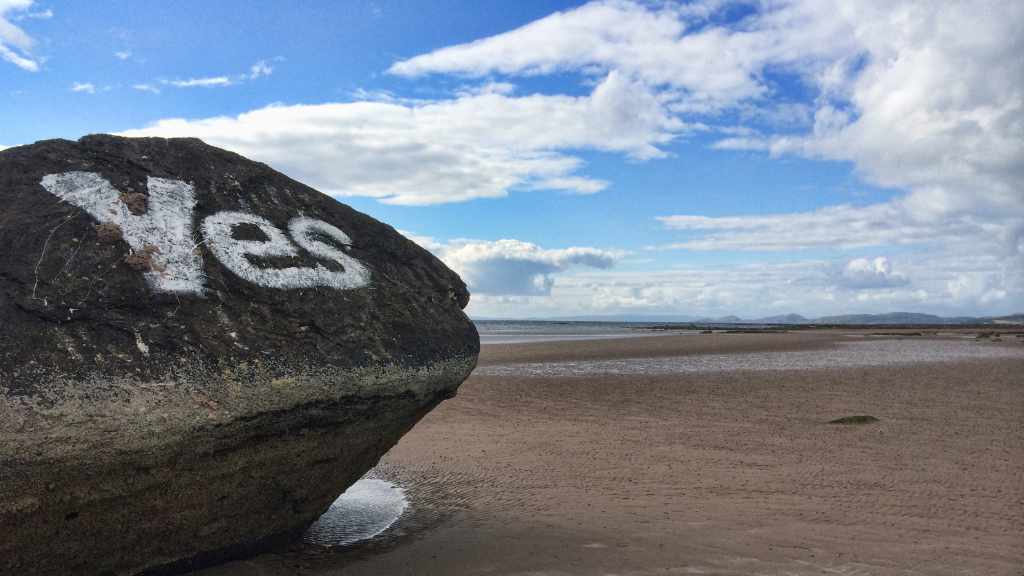 Picture of a beach with a large rock in the foreground with the word Yes painted on it