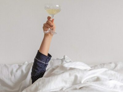 woman in lying in bed holding up a champagne glass