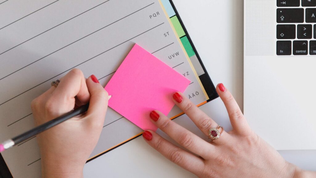 A woman's hand indexing a journal using a pink sticky note.