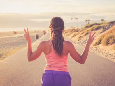 woman in fitness clothing walking away from the camera holding her hands up in the peace sign