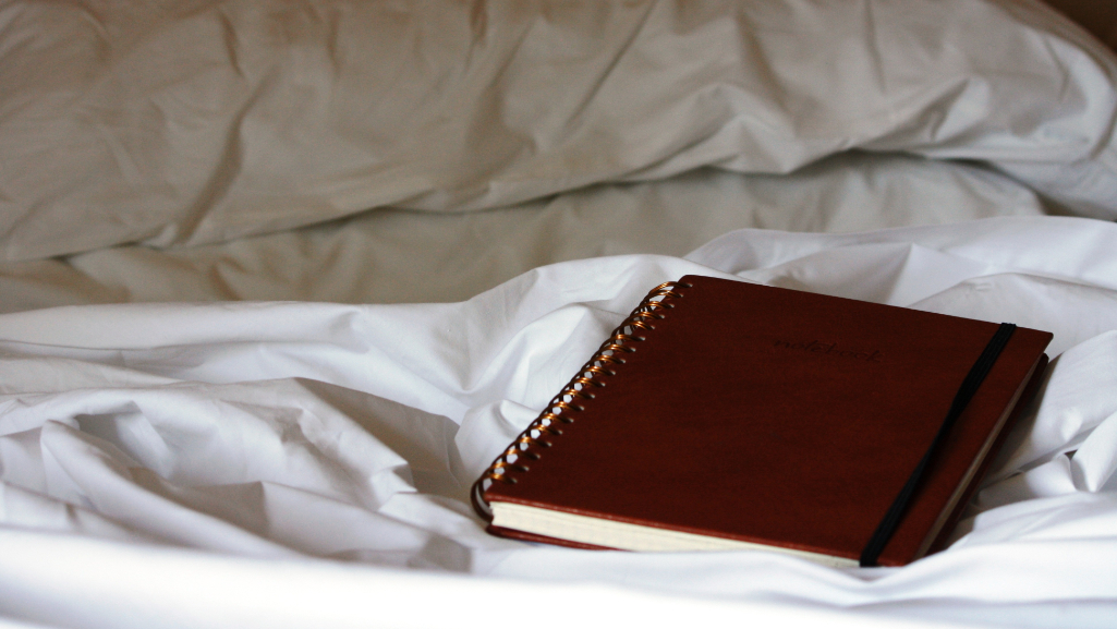 a brown spiral bound notebook on a bed