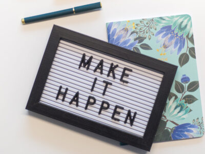 a sign that says make it happen lying on top of a flowery notebook