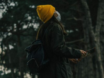woman in the woods with a rucksack and hat wearing facemask