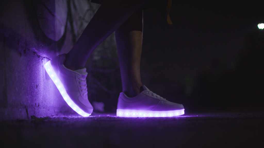 a pair of feet in white trainers that have lights in the soles which give the picture a purple tinge.