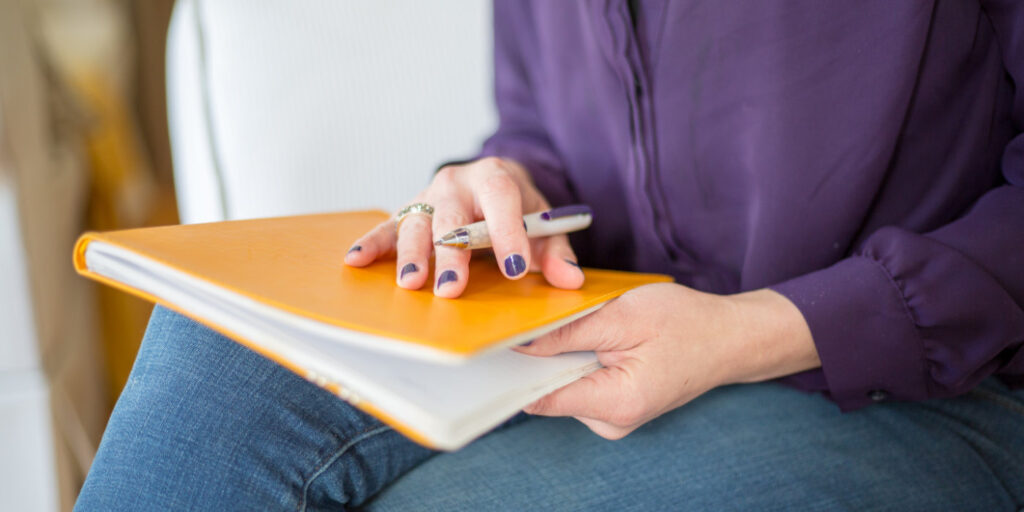 woman wearing a purple shirt holding a yellow notebook on her lap
