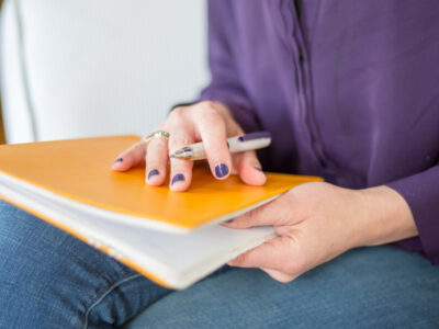 woman wearing a purple shirt holding a yellow notebook on her lap