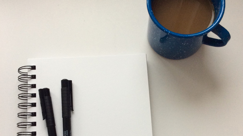 an open notebook with plain pages next to a blue cup of coffee